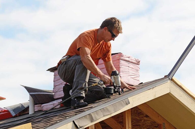 A person inspecting roof eaves for signs of pest damage on a two-story home in early spring.