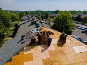 A roofer fits metal flashing around a plumbing vent pipe on a shingled roof.